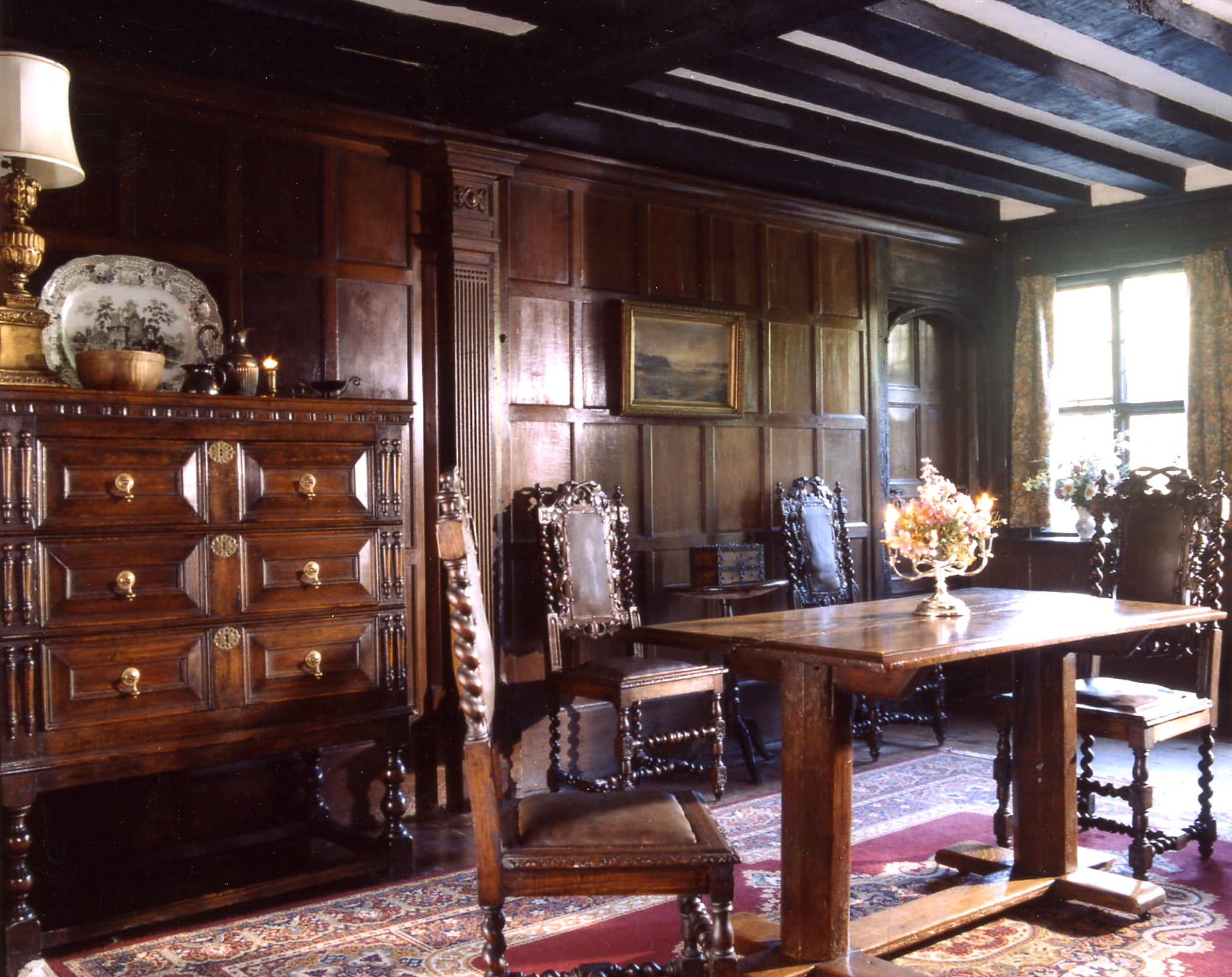 The entrance hall with wood paneled walls, a table and chairs and an ornate wooden tall boy
