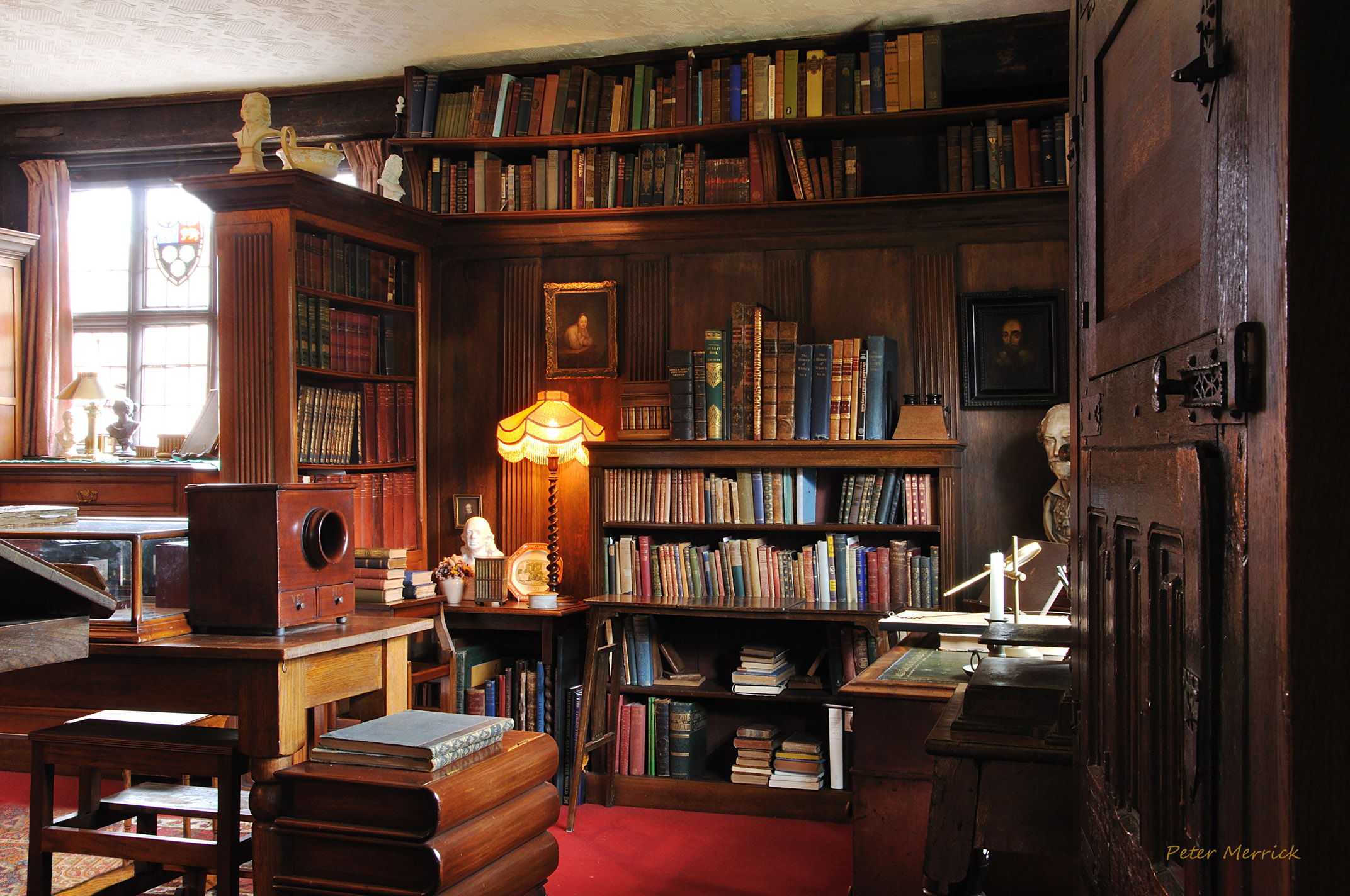the libary with wood paneled walls and bookcases and a cosy lit lamp