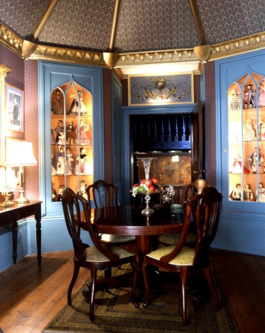 a compact octagonal room with a polished dining table and glass display cabinets containing ornamental figurines