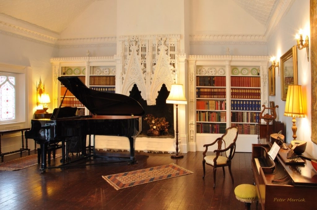 the victorian music room with a grand piano, ornate fireplace and bookcases